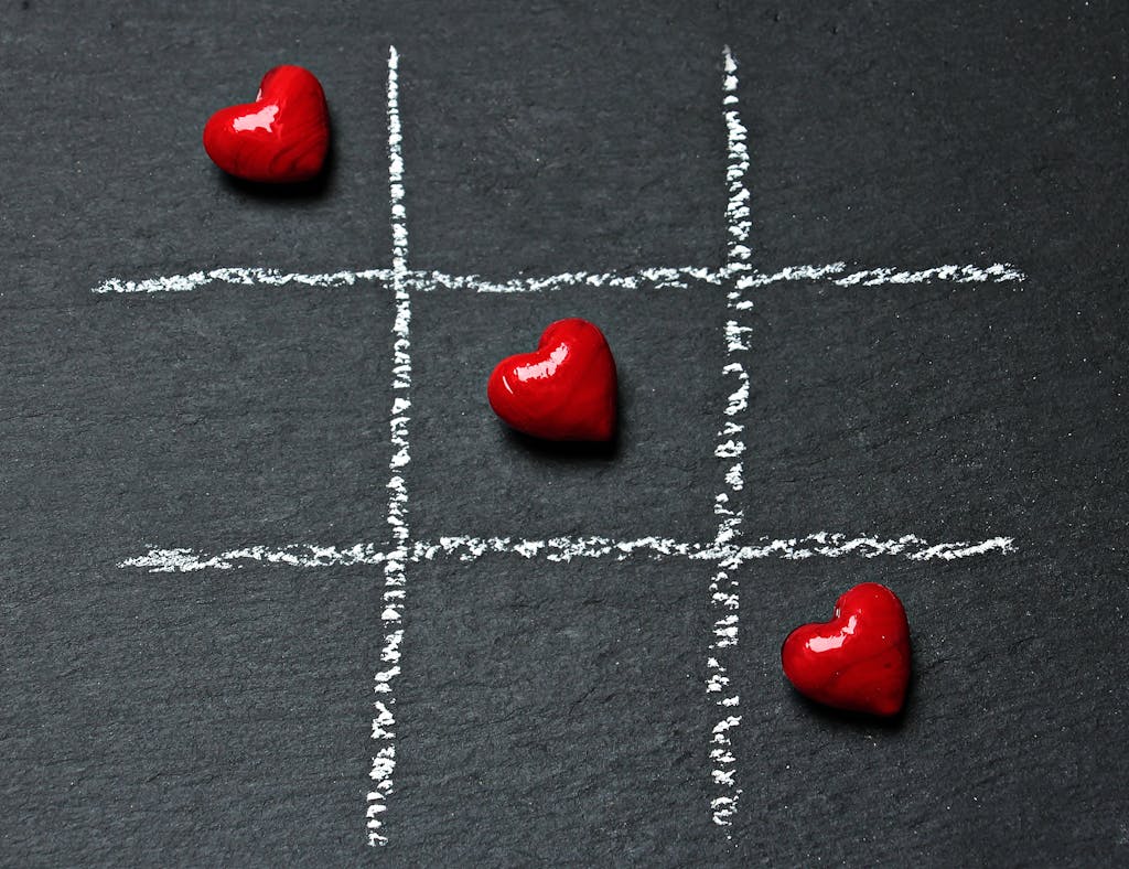 Tic tac toe board on black surface with red heart shapes symbolizing love and connection.