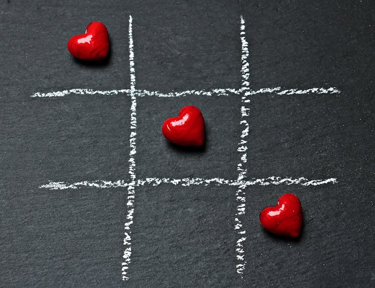 Tic tac toe board on black surface with red heart shapes symbolizing love and connection.